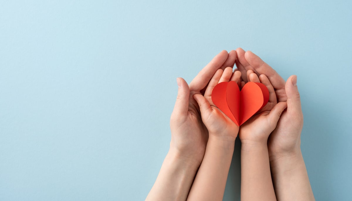 Adult and child hands holding a red heart, representing family care and compassion